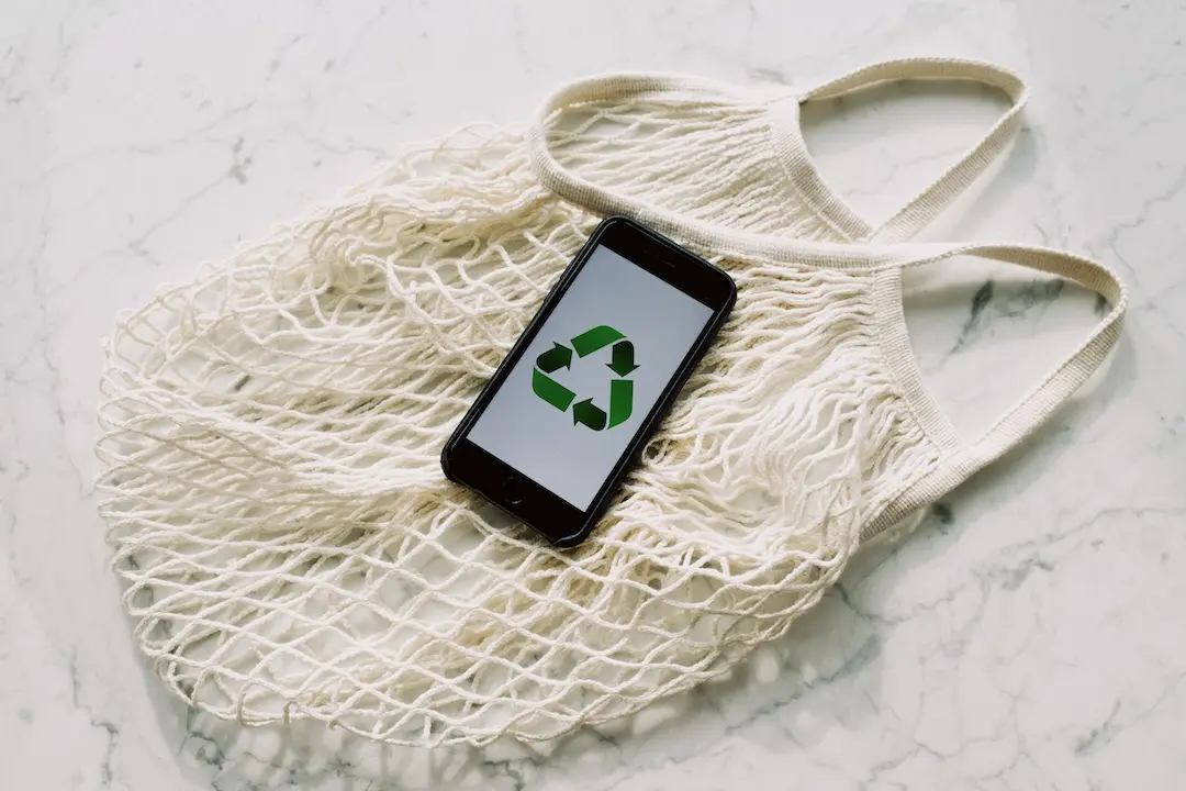 Reusable grocery bag with a cell phone showing a recycling logo for the article about upcycling vs recycling.